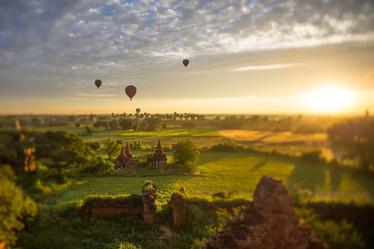 Hot air balloons float over the temples of Bagan at sunrise, with brick pagodas rising above the trees
