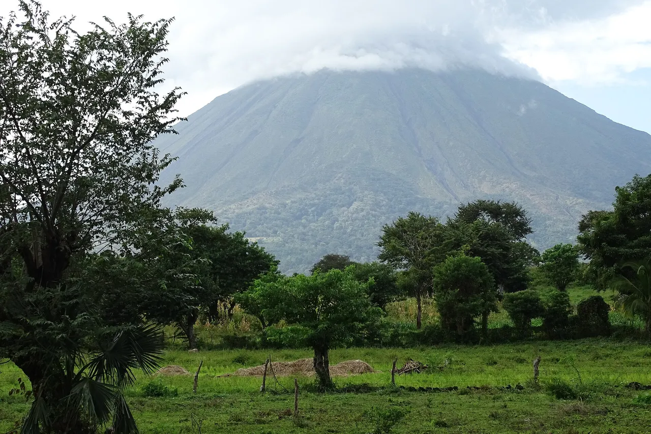 The cone of Concepción volcano, its top hidden in cloud, rises above green fields and trees on Ometepe Island in Lake Nicaragua