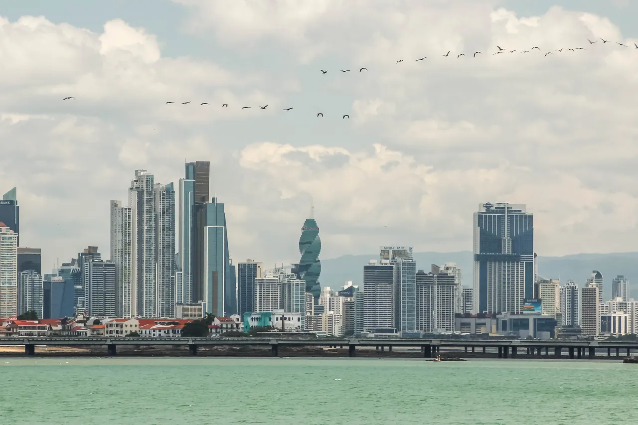 The glass towers of Panama City rise behind the red roofs of the old town, with pelicans flying over the Bay of Panama