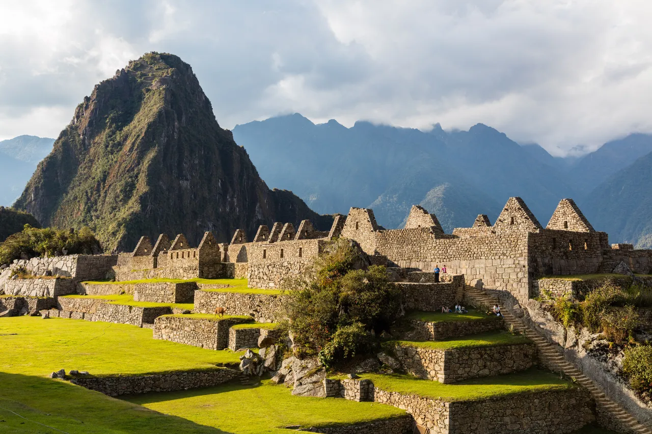 The stone ruins and green terraces of Machu Picchu, with the peak of Huayna Picchu and the Andes behind
