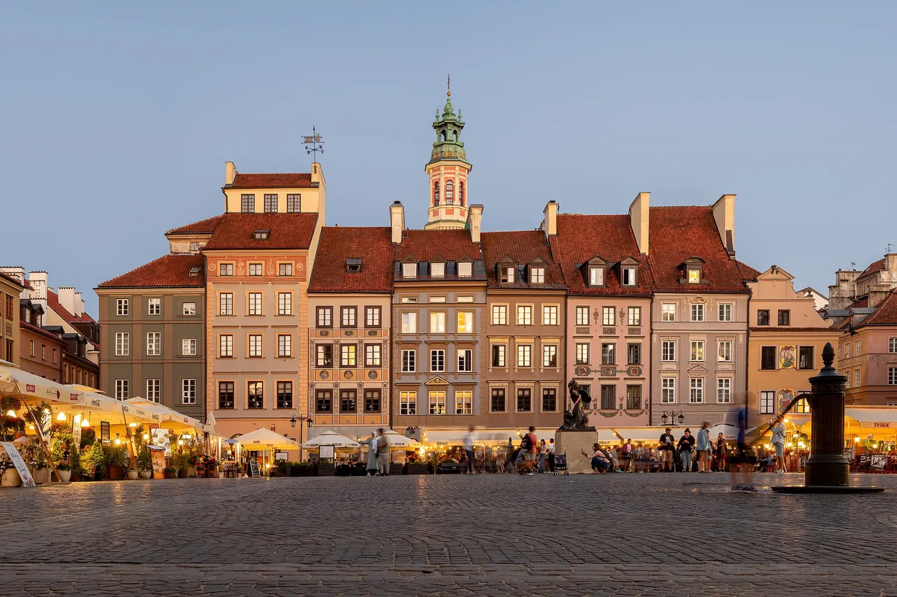 Colorful merchant houses on the Old Town Market Square in Warsaw at dusk, with café umbrellas lit below
