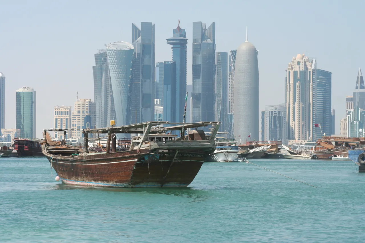 Doha's West Bay skyline of glass towers seen across turquoise water, with a wooden dhow moored in the foreground