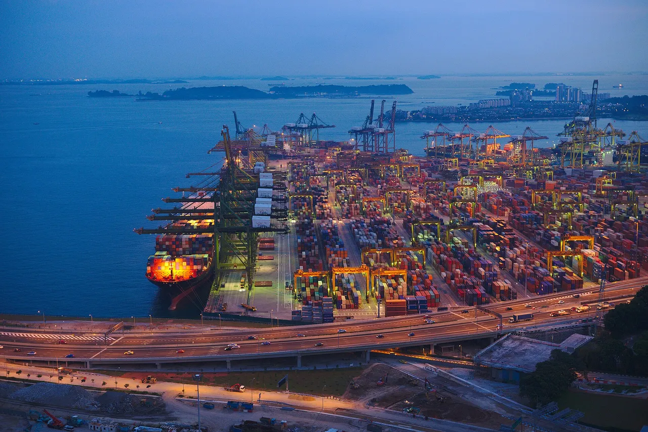 The Tanjong Pagar container terminal at dusk, with stacked containers, cranes, a lit container ship and the sea and islands beyond
