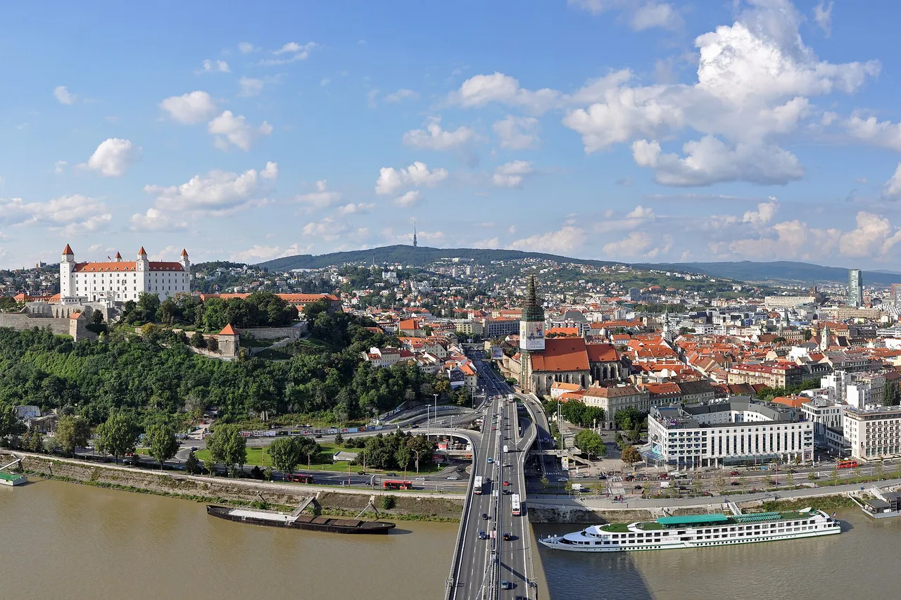Bratislava from above, with the white castle on its hill, the old town and its cathedral spire, a highway bridge and river boats on the Danube