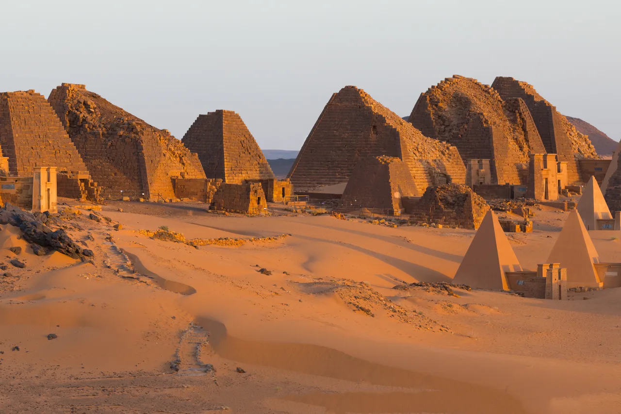 The steep pyramids of Meroe at sunrise, half buried in orange sand dunes