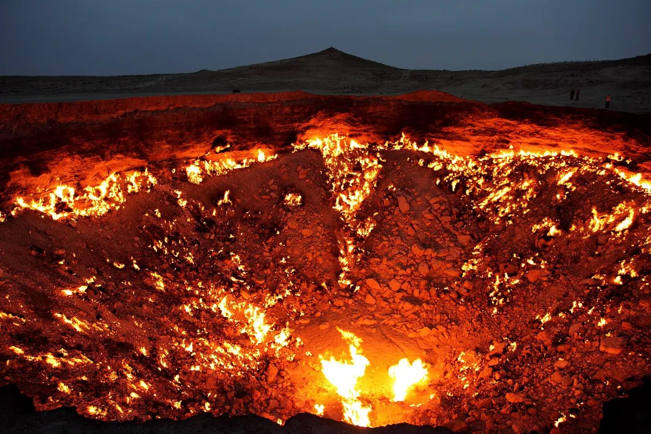 Flames burning across the rocky floor and walls of a huge round crater in the desert at dusk