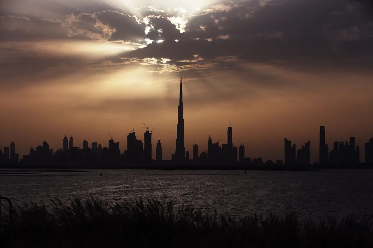 The Burj Khalifa and the Dubai skyline in silhouette under a cloudy sunset sky