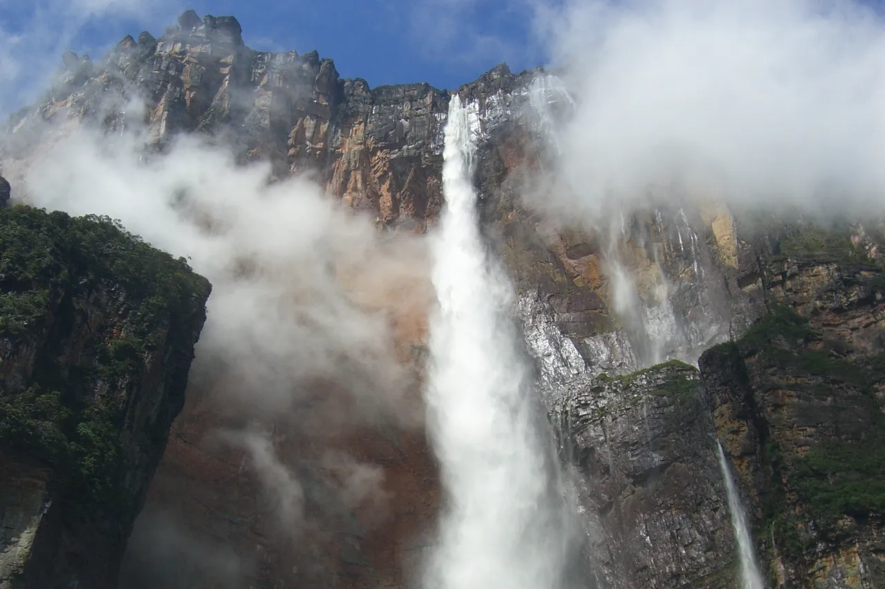 Angel Falls dropping from the cliffs of Auyán-tepui into the forest, with clouds drifting across the rock face