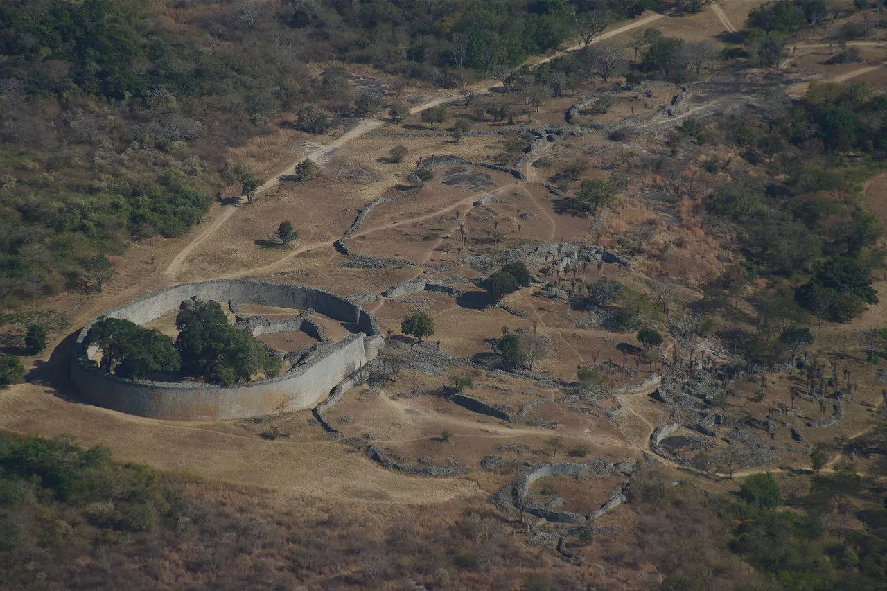 Aerial view of the ruins of Great Zimbabwe, with the curved stone wall of the Great Enclosure surrounded by dry grass and trees