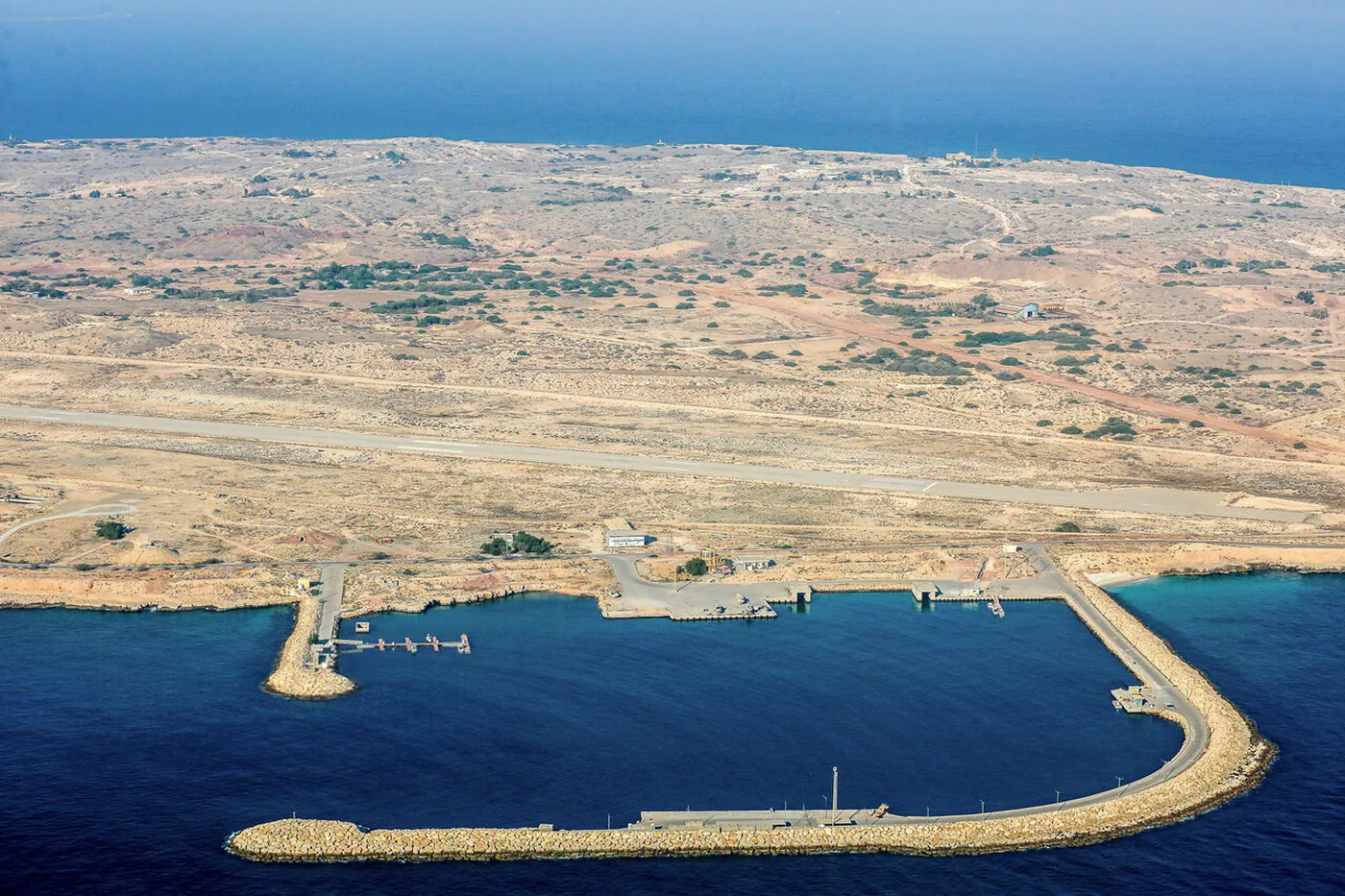 Aerial view of Abu Musa, with a harbor and its long breakwater in the foreground and a runway across the flat island behind it