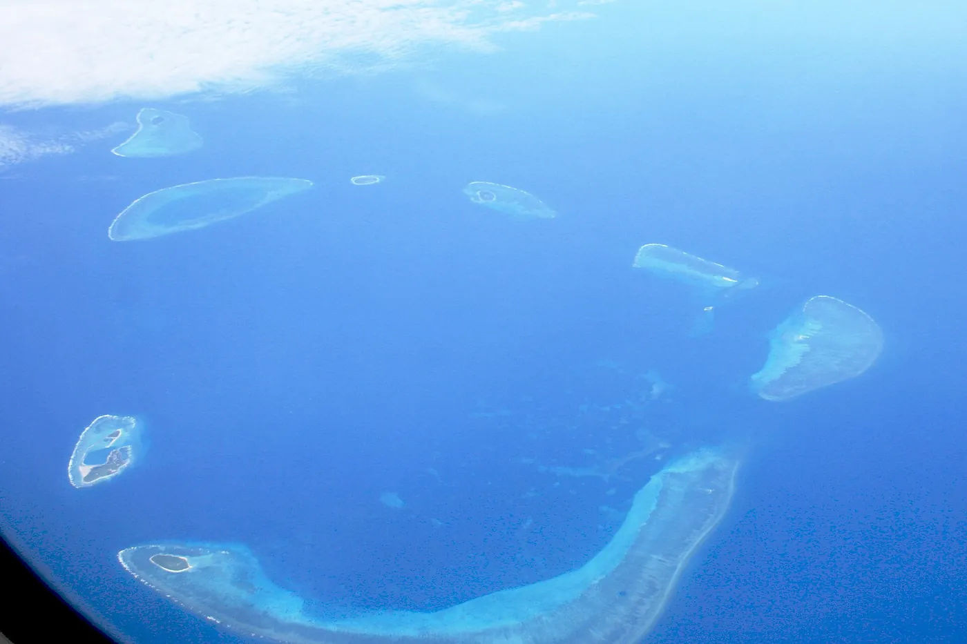 Turquoise reefs and small sandy islands of the Crescent Group in a deep blue sea, seen from a plane window