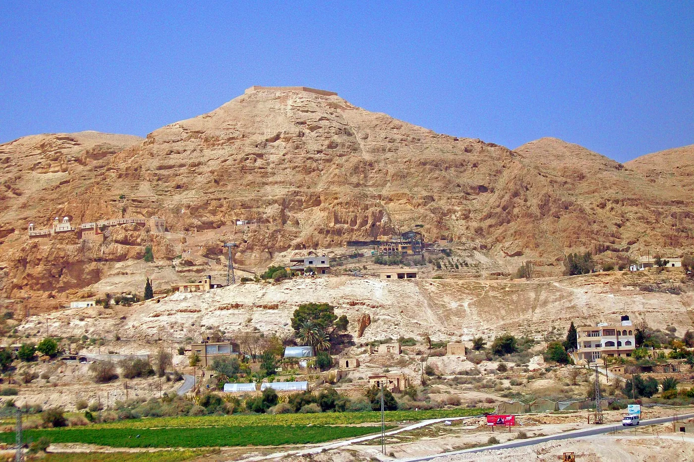 Houses and fields of Jericho below a bare, rocky mountain with a monastery on its slope
