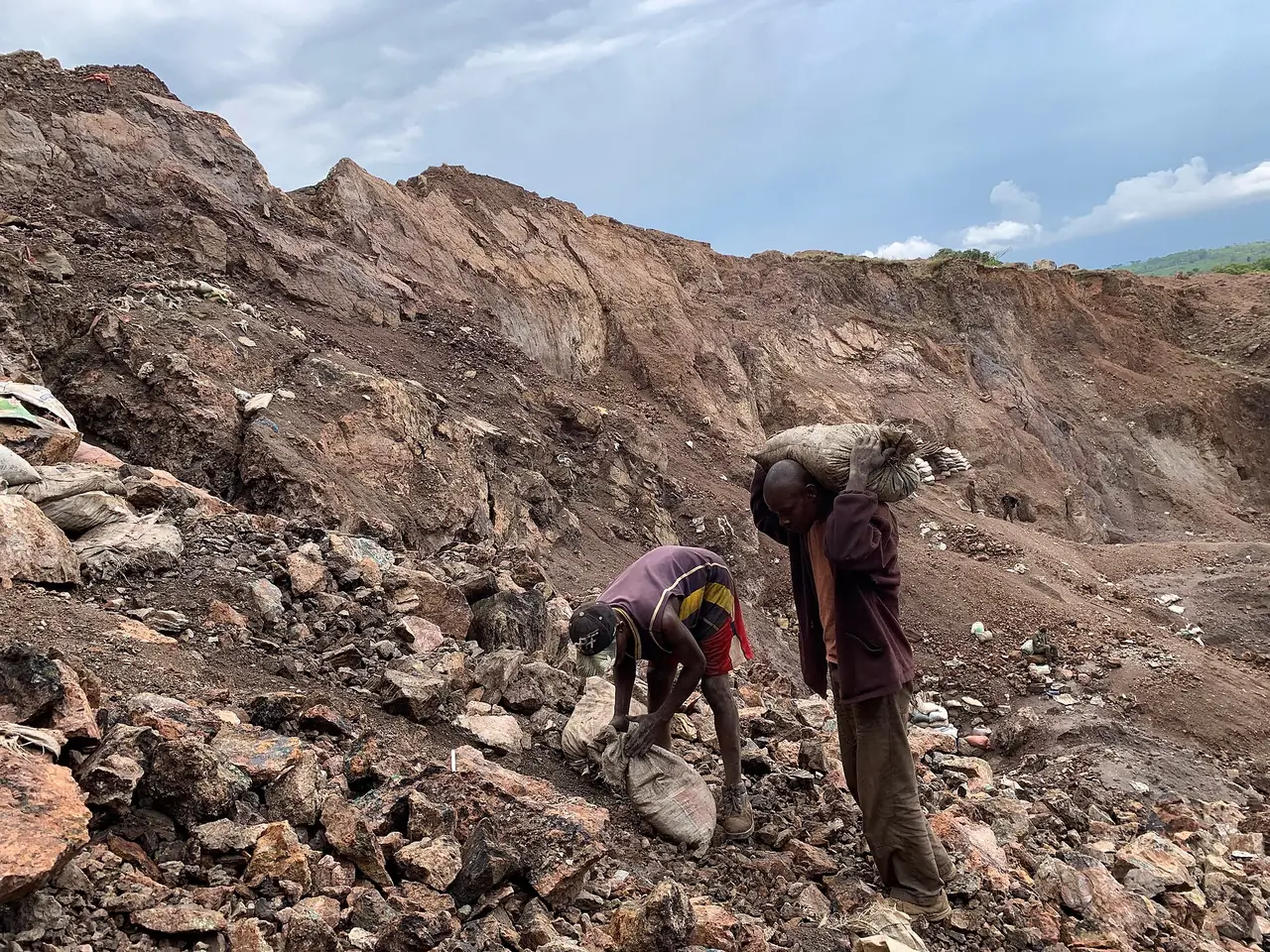 Two artisanal miners digging for cobalt ore on a rocky slope in DR Congo
